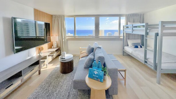 A hotel room with a TV, bunk beds, a sofa, a small table with a plant, and a view of the ocean. - 40F-High Floor-Stunning Ocean View-1 Bedroom Condo-Waikiki Beach (Honolulu)