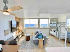 Een moderne hotelkamer met een groot raam, een flatscreen televisie, een bank, een zithoek en stapelbedden.