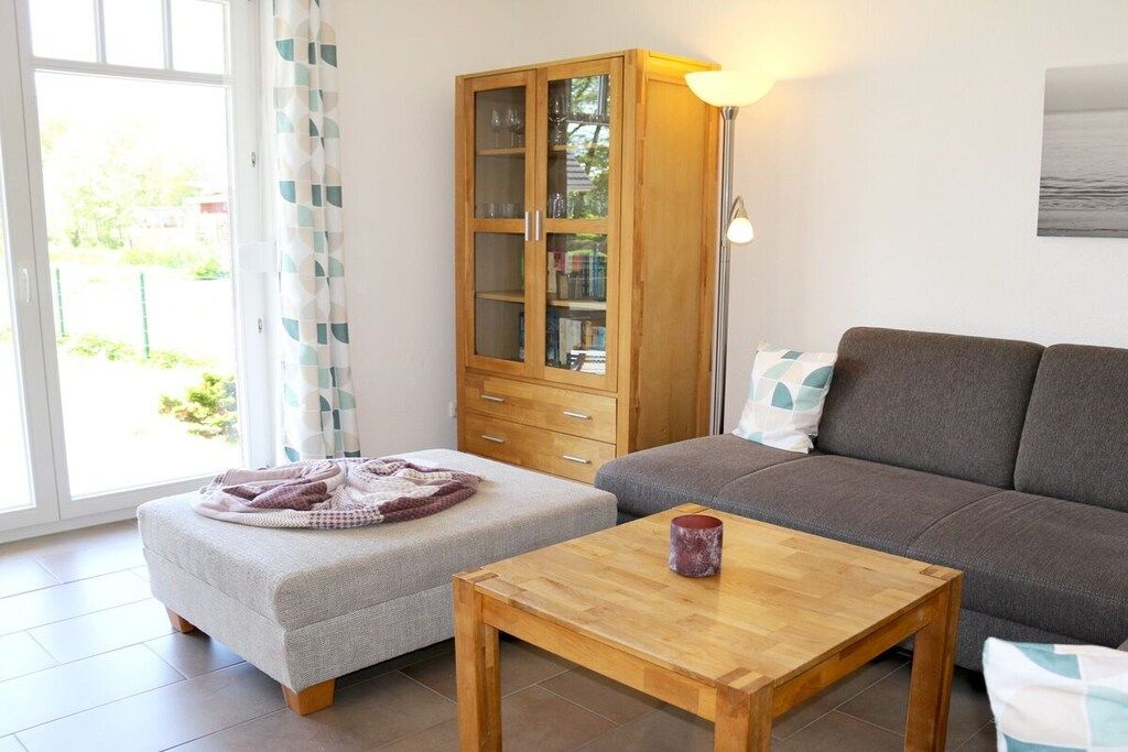 Ein Wohnzimmer mit einer Couch, Hocker und einem Holztisch. Es gibt ein Schrank mit Glastüren und eine Lampe.