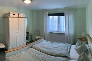 A bedroom with a bed, a wardrobe, a chair, a table, and a window with curtains. - Holiday apartment MEERzeit (Rerik)