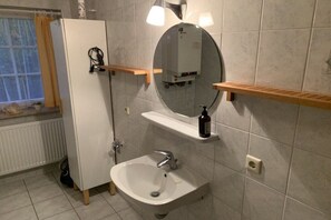 A bathroom with a white sink, a mirror, and a heater on the wall. - Holiday apartment MEERzeit (Rerik)