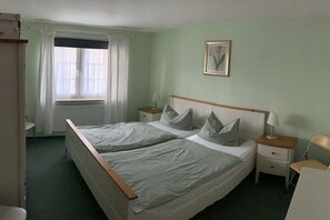 A double bed with a wooden frame, two bedside tables, a window with curtains, and a framed picture on the wall. - Holiday apartment MEERzeit (Rerik)