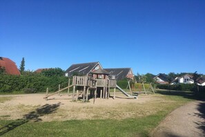 Un terrain de jeux avec une structure en bois et un toboggan, entouré de pelouse et sous un ciel dégagé.
