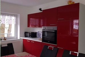 A kitchen with red cabinets, a microwave, an oven, and a window with curtains. - Holiday apartment with 1 bedroom (Sassnitz)
