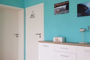 A room with a white door, a white cabinet with drawers, and a turquoise wall. - Holiday apartment with 1 bedroom (Sassnitz)