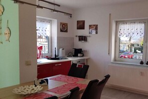A compact kitchen with a dining area, a window with curtains, and a view of the outside. - Holiday apartment with 1 bedroom (Sassnitz)