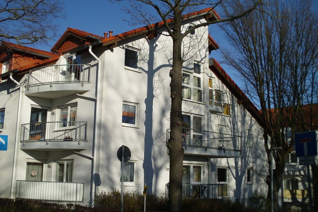A multi-story residential building with balconies, a visible tree, and a clear sky.