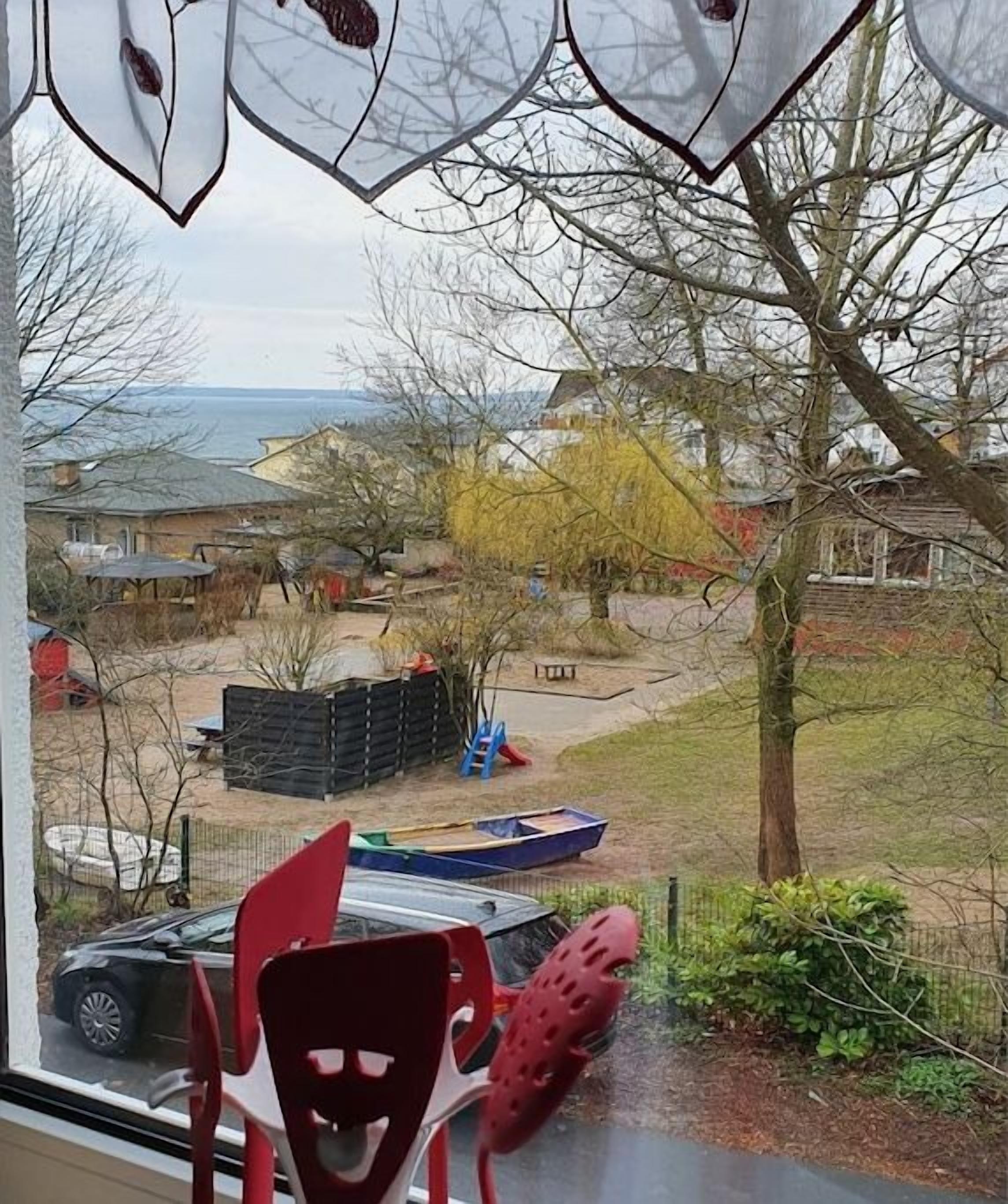Blick aus einem Fenster auf einen Spielplatz mit Rutsche und umzäunter Fläche.