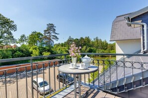 A balcony with a table set for tea, a flower vase, and a view of a parking area and greenery. - Holiday apartment in Benz with swimming pool (Benz)