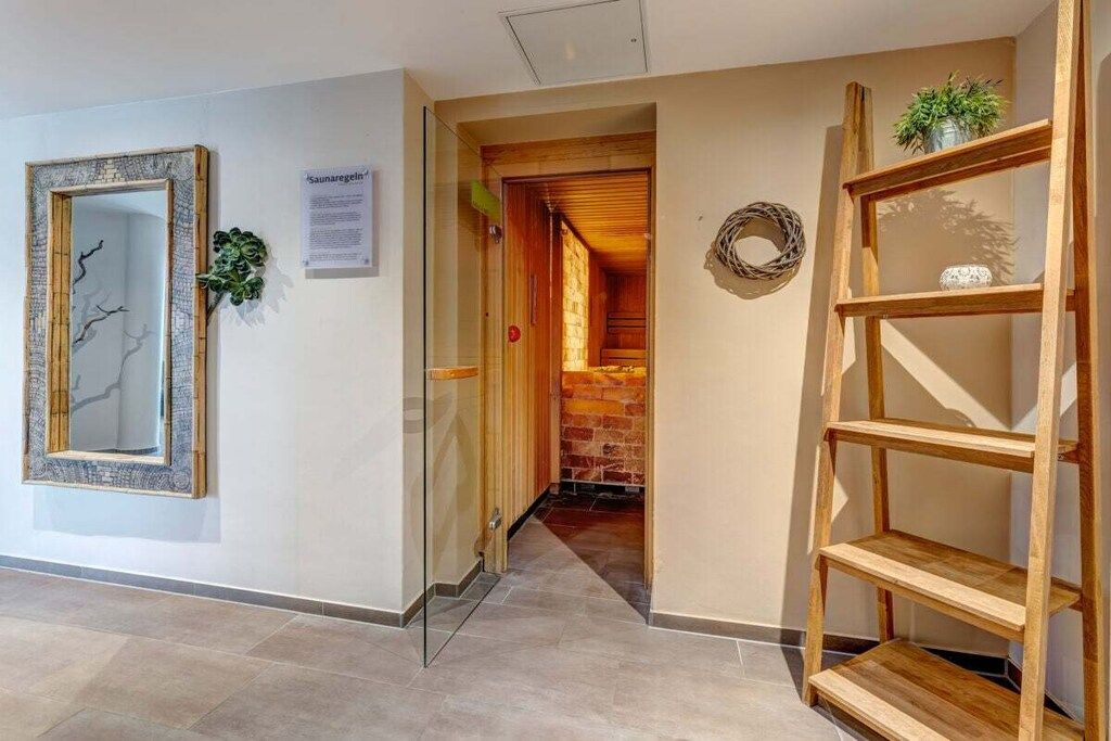 Ein Flur mit einer Glastür, die zu einem Raum mit Backsteinwand und Holztür führt. Eine Holzregaleinheit mit einer Pflanze darauf ist ebenfalls zu sehen.