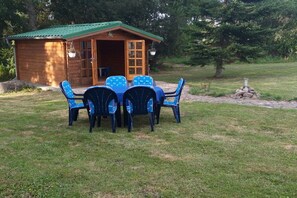 Eine Holzhütte mit einem grünen Dach, einem Tisch mit Stühlen und einer Steinstruktur im Hintergrund.