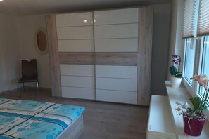 Une chambre à coucher avec un lit, une armoire, une chaise et une fenêtre avec des plantes.