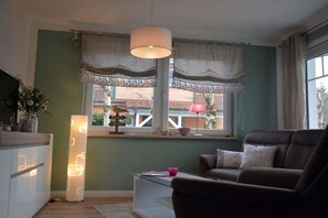 A living room with a sofa, a table with a pink bowl, a lamp, and a window with curtains. - Holiday apartment with 1 bedroom (Ostseeheilbad Zingst)