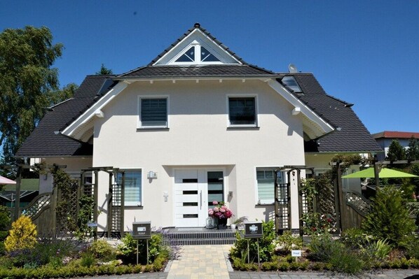 A two-story house with a front porch, a small garden, and a clear sky. - Holiday apartment with 1 bedroom (Ostseeheilbad Zingst)