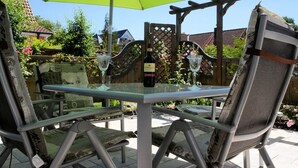 Een terras buiten met een tafel, stoelen, een fles wijn en een groene parasol.