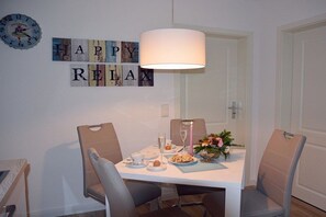 A dining area with a table set for two, a clock on the wall, and a 'HAPPY RELAX' sign. - Holiday apartment with 1 bedroom (Ostseeheilbad Zingst)