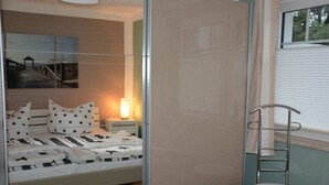 Een slaapkamer met een bed, nachtkastje, lamp en een stoel.
