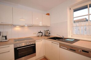 Eine moderne Küche mit weißen Schränken, einem Edelstahlbackofen, einem Geschirrspüler und einem Fenster mit Blick.