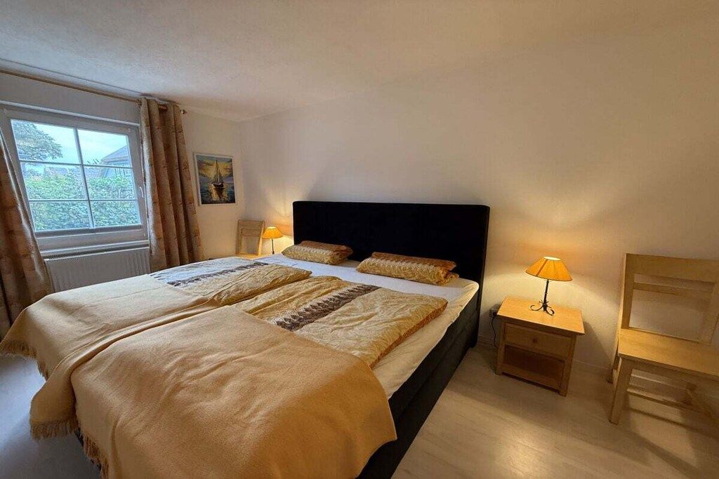 A bedroom with a bed, two bedside tables, a chair, a window with curtains, and a painting on the wall.