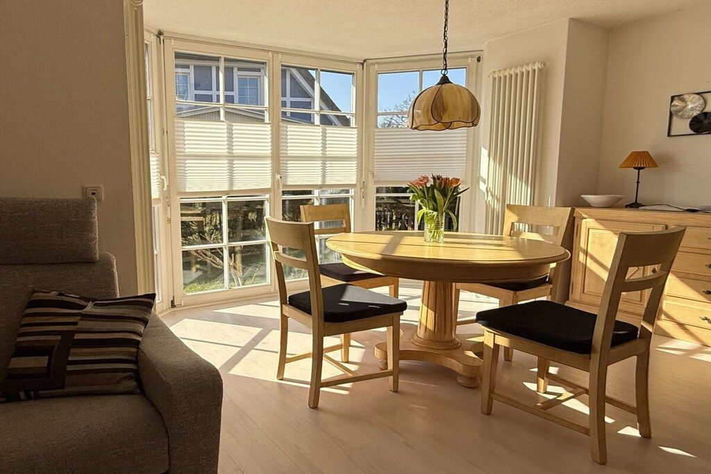 A dining area with a round table and chairs, a sofa, and a window with blinds.