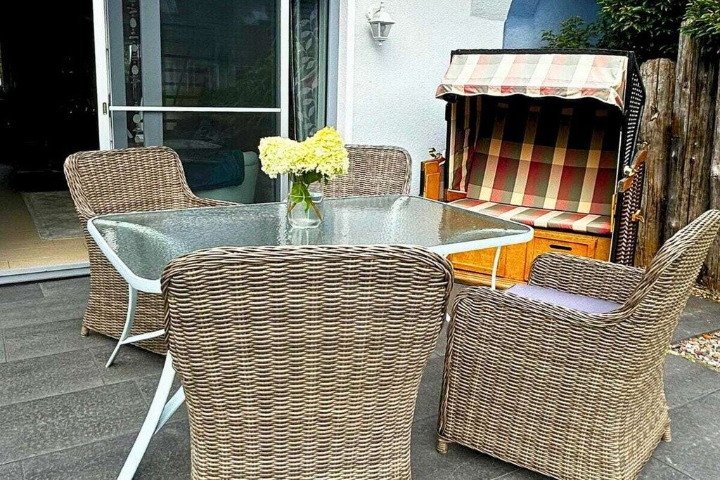 En patio med fletmøbler, et glasbord og en bænk med ternet betræk.