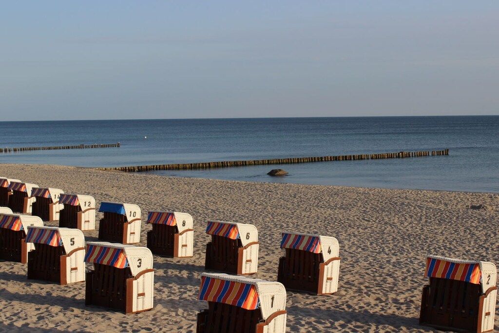 Beach huts numbered 1-12, wooden beach chairs, and a wooden jetty extending into the sea.