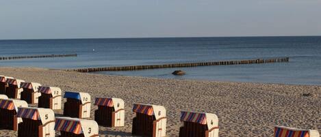 Beach huts numbered 1-12, wooden beach chairs, and a wooden jetty extending into the sea.
