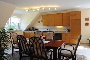 Ein Essbereich mit Holztisch und -stühlen, eine Küche mit Holdekor und ein Fenster mit Vorhängen.