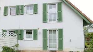 Um edifício de dois andares com persianas verdes nas janelas, uma porta branca e um caminho de tijolos que leva à entrada.