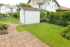 A residential property with a paved driveway leading to a white garage, surrounded by well-maintained grass and shrubs. - Dune Resort Lindenweg (Karlshagen)