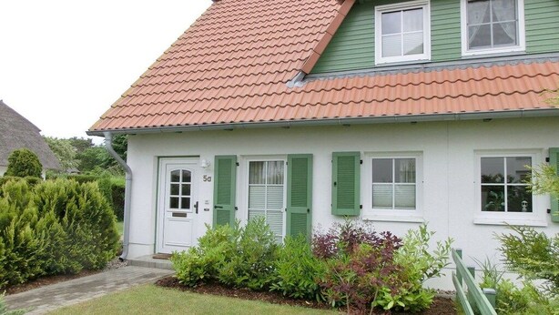 Uma casa branca com persianas verdes e telhado de telhas vermelhas.