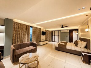 Ein modernes Hotelzimmer mit einer Couch, einem Glastisch, einem Bett, einem Fernseher und einem Deckenventilator.