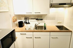 A compact kitchen with white cabinets, a stainless steel sink, a black coffee maker, and a Bosch range hood. - Holiday apartment with 1 bedroom (Seebad Ahlbeck)