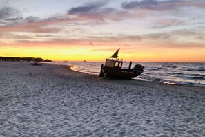 Een strand met een boot in het zand en de oceaan op de achtergrond.