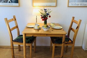 A wooden dining table with chairs, a vase with flowers, a lamp, and plates with cups. - Holiday apartment with 1 bedroom (Seebad Ahlbeck)