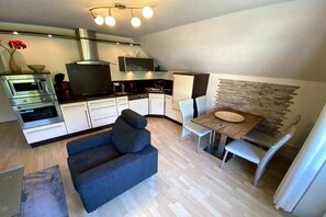 Ein kompakter Wohnraum mit Küchenzeile, einem Essbereich mit Tisch und Stühlen sowie einer Couch.