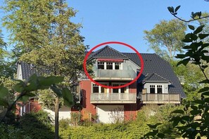 Ein zweistöckiges Haus mit Balkon, umgeben von Bäumen und Pflanzen.