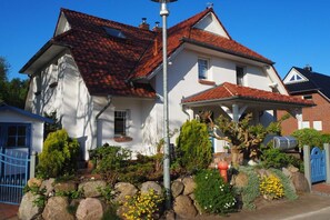 Une maison à deux étages, avec un toit recouvert de tuiles rouges, des murs blancs et un porche à l’avant.