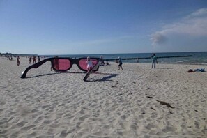 Une plage avec une paire de lunettes de soleil posée sur le sable, des personnes à l’arrière-plan et un ciel dégagé.