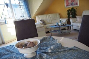 A cozy living room with a white sofa, a coffee table, and a bowl of food on a patterned tablecloth. - Holiday apartment with 1 bedroom (Zingst)