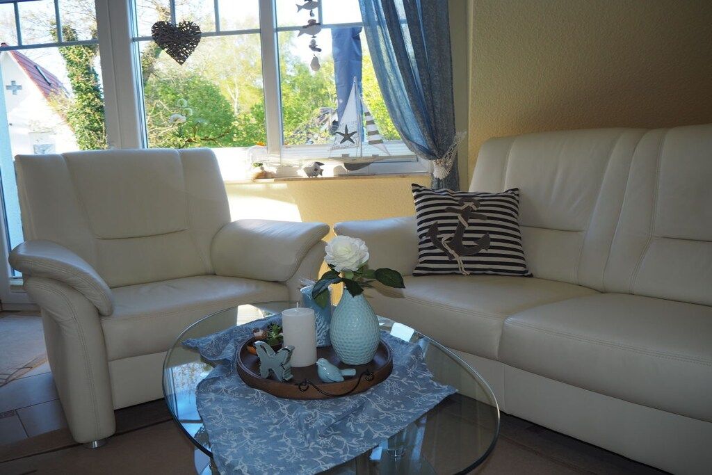 A living room with a beige sofa, a glass coffee table with decorative items, and a window with curtains.