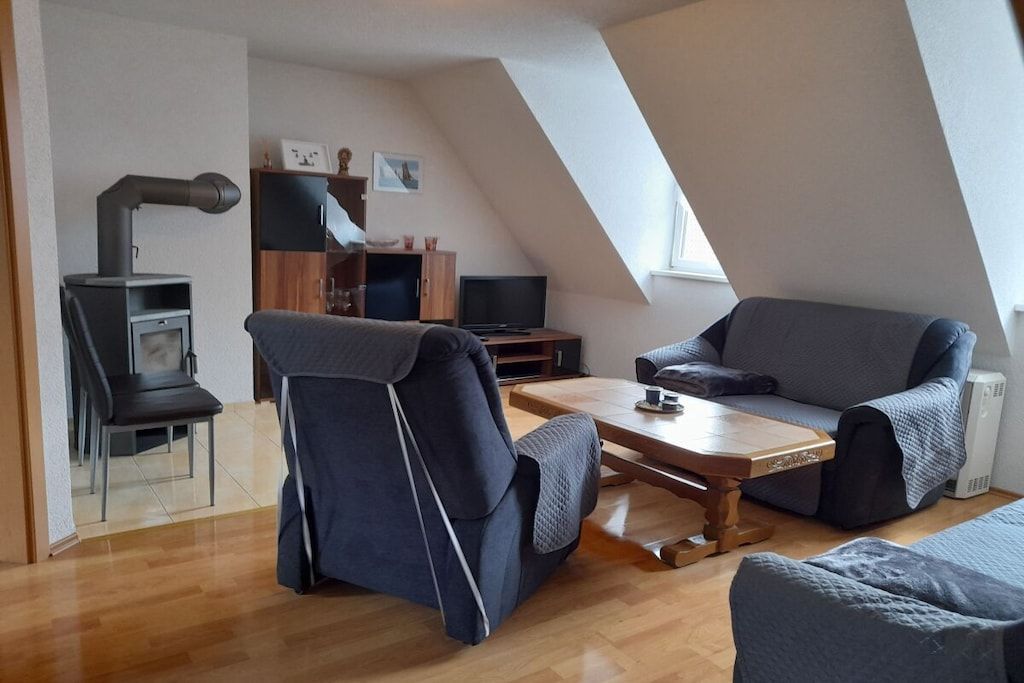 Una sala de estar moderna con sofá, sillón, mesa de centro de madera, televisor y chimenea.