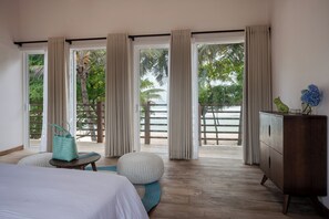 Una habitación con cama, una mesita, un armario y ventanas amplias con cortinas.