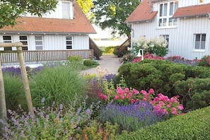 Ein Gartenweg führt zu einer Reihe von Häusern, begrenzt durch einen Holzzaun, mit verschiedenen blühenden Pflanzen.