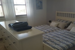 Ein Schlafzimmer mit einem Bett, einem Nachttisch, einer Lampe und einem Fenster mit Vorhängen.