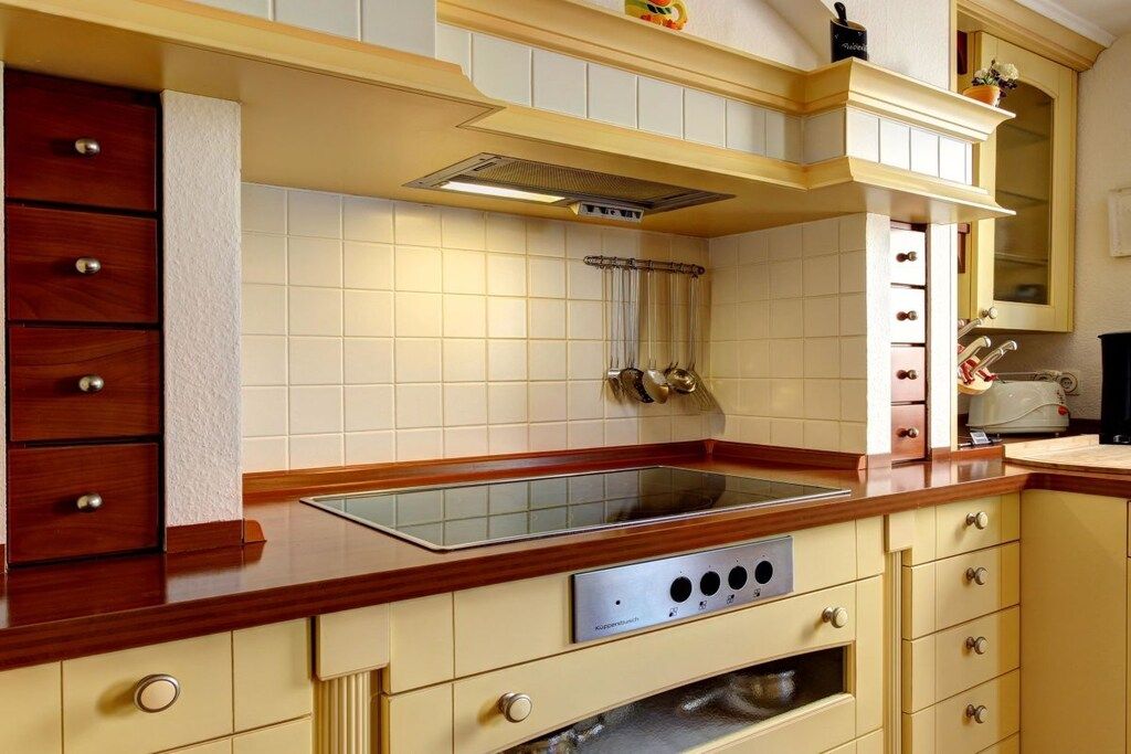 A kitchen with a wooden countertop, a built-in stove, and white tiled walls.