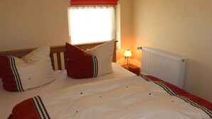 A hotel room with a bed, a window with curtains, a bedside lamp, and a radiator. - Holiday apartment Donnerkeil (Sassnitz)