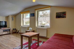 A living room with a television, a wooden table, a red sofa, and two windows with curtains. - Holiday apartment Donnerkeil (Sassnitz)