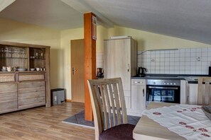 A compact kitchen with a refrigerator, oven, and a dining area with a chair and table. - Holiday apartment Donnerkeil (Sassnitz)