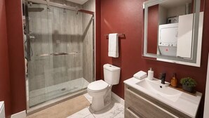 A modern bathroom with a glass-enclosed shower, a white toilet, and a vanity with a mirror. - Moody Designer Retreat Near Greenville & Downtown (Dallas)